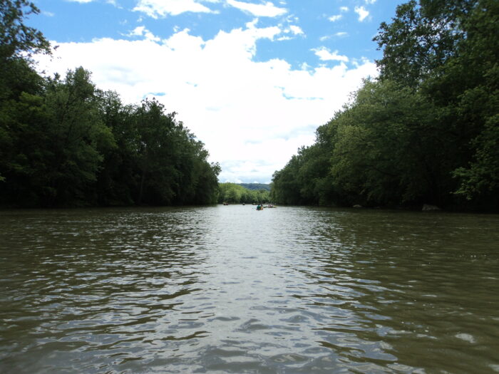Canoes float under a blue sky on the Juniata River. The river's watershed, the Juniata Watershed, encompasses 3,400 square miles, approximately two-thirds of which is forested.