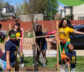 a group of young people celebrate near a recently planted tree in a city neighborhood