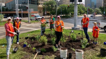 Several smiling volunteers dressed in orange safety vests work in Libarty Avenue garden in downtown Pittsburgh